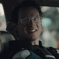 a man wearing glasses sitting in the back seat of a car