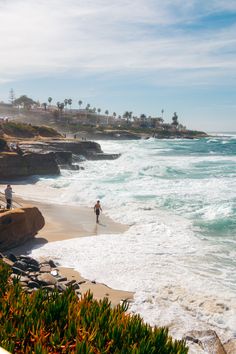 two people are walking along the beach near the water's edge with waves crashing on them