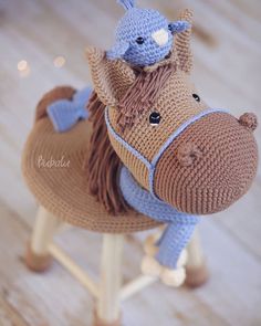 a knitted horse sitting on top of a wooden stool with a blue hat on it's head