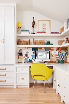 a desk with a computer on top of it next to a yellow chair and bookshelf