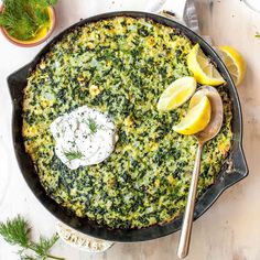 a pan filled with spinach and lemons on top of a white table next to silverware