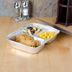 an aluminum foil container filled with different types of food next to a knife and salt shaker