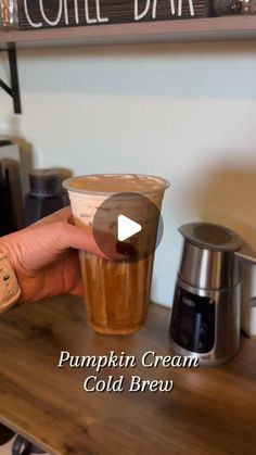 a person holding up a cup of coffee on top of a wooden table next to an espresso machine