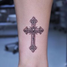 a small cross tattoo on the foot of a woman's right leg, with an intricate design