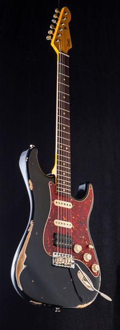 an electric guitar hanging from the side of a black wall with a red and yellow neck