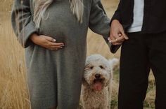 a man and woman holding hands while standing next to a small dog in a field