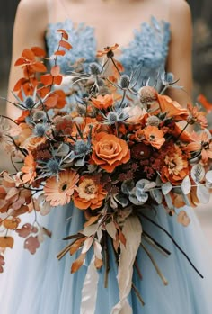 a woman in a blue dress holding a bouquet of orange and grey flowers on her wedding day