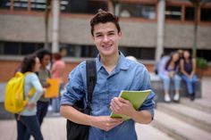 a young man standing in front of some stairs holding a folder and smiling at the camera