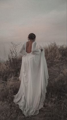 a woman in a white dress is standing on a hill with her back to the camera