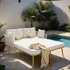 a white couch sitting next to a swimming pool with palm trees in the back ground