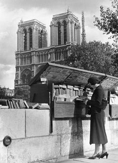 a woman standing next to a book stand on the side of a road in front of a cathedral