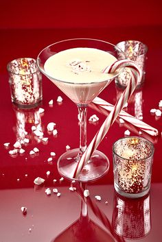 a candy cane in a martini glass next to two shot glasses filled with white chocolate and sprinkles