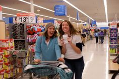 two women are pushing a shopping cart in a store and one is holding a cell phone