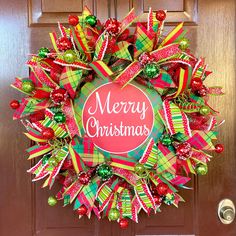 a merry christmas wreath on the front door with red, green and yellow ribbon around it