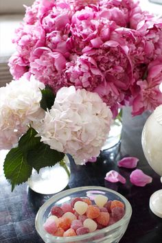 pink and white flowers are in vases on a table next to a bowl of candy