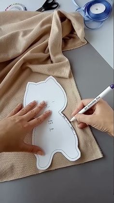 someone is cutting out a paper cutout for a teddy bear ornament on a piece of fabric