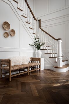 a wooden bench sitting in the middle of a room next to a stair case and white walls