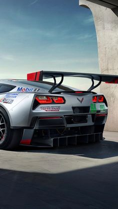 a silver sports car parked in front of a concrete structure with its hood open and the top down