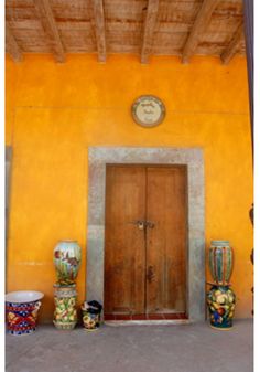 a yellow building with vases and a clock on the wall