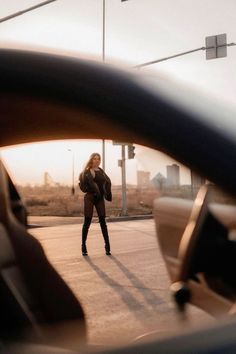 a woman walking across a street next to a traffic light with her hand on the steering wheel