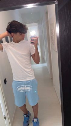 a young man taking a selfie in the mirror with his cell phone while wearing blue shorts