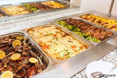 several trays of different types of food sitting on a counter in a buffet area