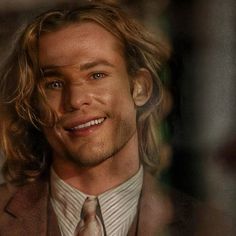 a man with long hair wearing a suit and tie looking at the camera while smiling