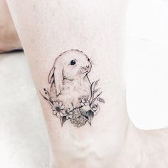 a small rabbit tattoo on the ankle with daisies and flowers around it's ankles