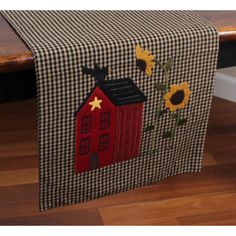 a table runner with sunflowers and a red barn on it, sitting on a wood floor