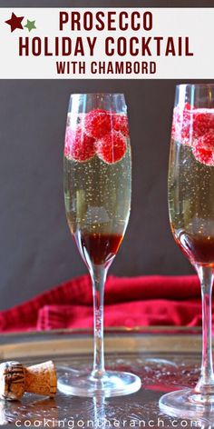 two champagne flutes with raspberries in them sitting on a table next to a cork