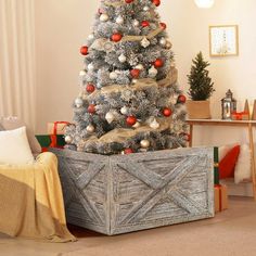 a christmas tree in a wooden crate with ornaments on it and a blanket draped over the top