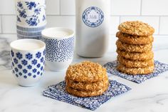 some oatmeal cookies are stacked on blue napkins next to milk bottles