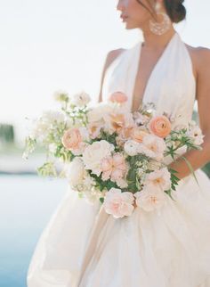 a woman in a white dress holding a bouquet of flowers near the water's edge