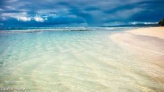 the water is crystal clear and there are clouds in the sky over the sand beach