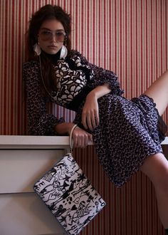 a woman leaning against a wall with her legs on the counter holding a handbag