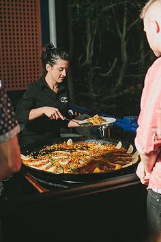 three people standing around a large pan of food