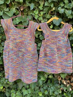 two knitted dresses hanging on a clothesline in front of some green plants and leaves