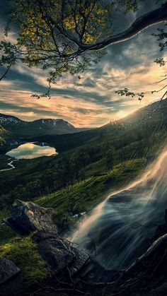 a waterfall in the middle of a lush green forest under a cloudy sky at sunset