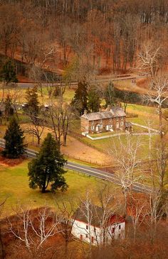 an aerial view of a farm house surrounded by trees and grass with a road in the foreground