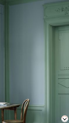 a chair sitting next to a table in front of a green painted wall and door