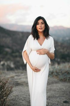 a pregnant woman in a white dress poses for a photo