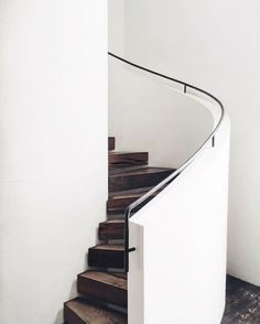 a spiral staircase with wooden steps in a white room next to a wall and floor