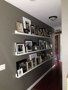 a wall filled with lots of framed pictures on top of white shelves next to a wooden floor