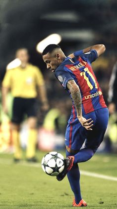 a man kicking a soccer ball on top of a field with other people in the background