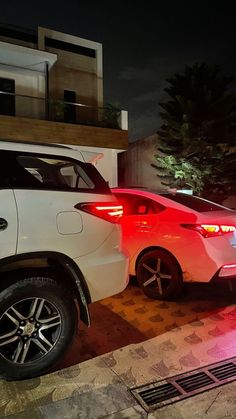 two cars parked next to each other in front of a building with lights on at night