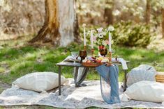 a picnic table with food and drinks on it in the middle of a forest area