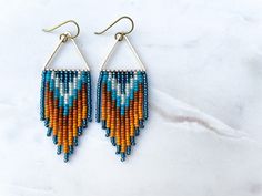 two pairs of beaded earrings with orange, blue and white designs on them sitting on a marble surface