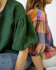 two women sitting on the ground with their backs to each other, one wearing a green top