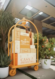 an orange cart with wine bottles on it in front of a building and potted plants