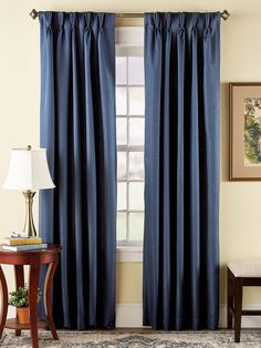 a living room with blue curtains and a table in front of the window that has a lamp on it